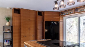 Una cucina moderna con mobili in legno, un frigorifero nero, un tavolo da pranzo con sedie e una finestra vista alberi.