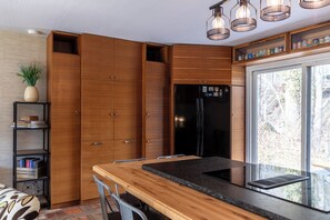 A modern kitchen with wooden cabinets, a black refrigerator, a dining table with chairs, and a window with a view of trees. - Ski, Hike, and Relax by the Creek - Hot Tub, Creek Access, Sleeps 11 (Banner Elk)