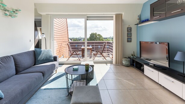 Una sala de estar moderna con sofá, una mesa de centro, televisor y un balcón con mobiliario exterior.
