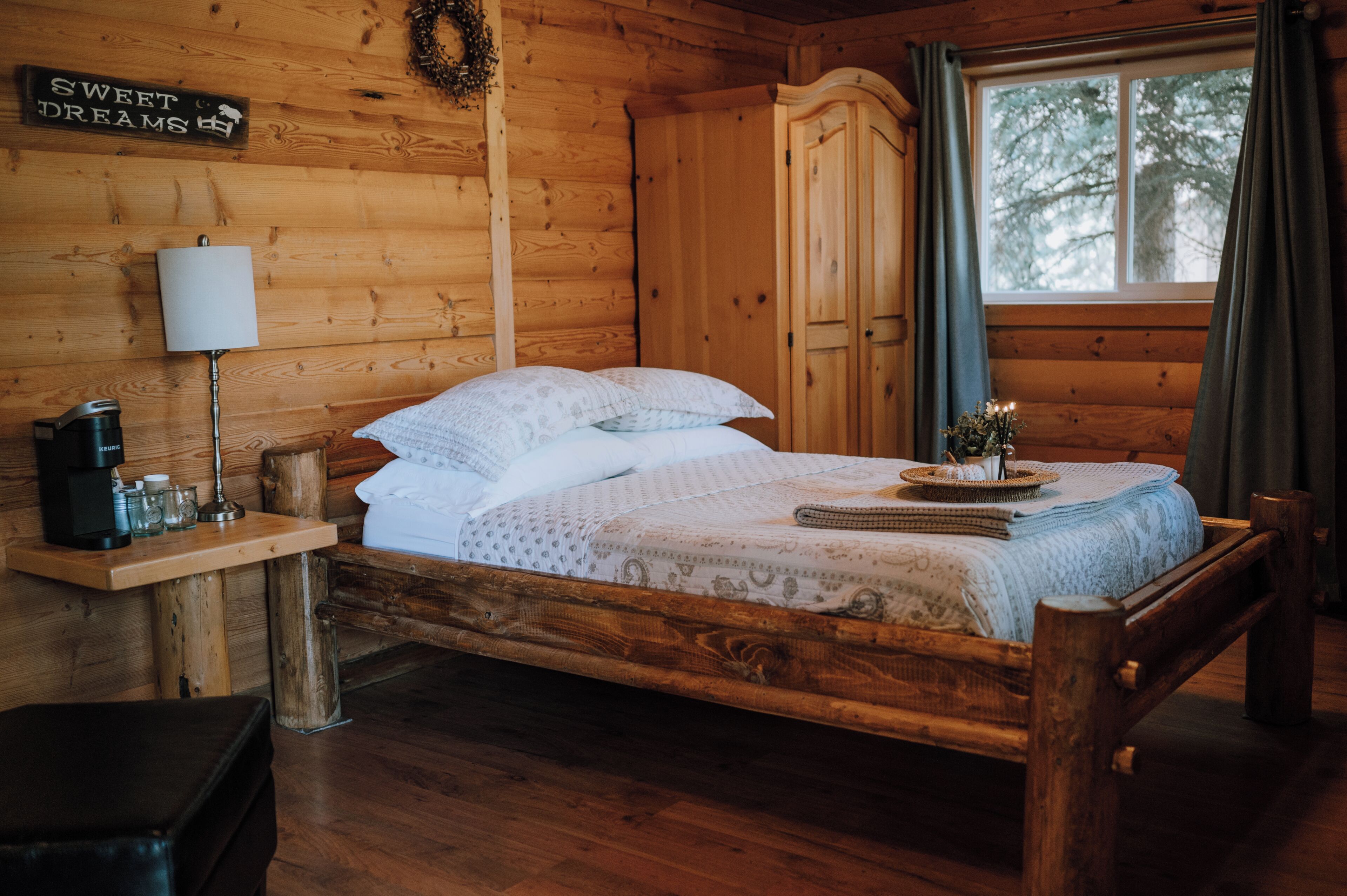 Een slaapkamer in een houten hutje, met een bed, een nachtkastje, een lamp en een bord aan de muur.