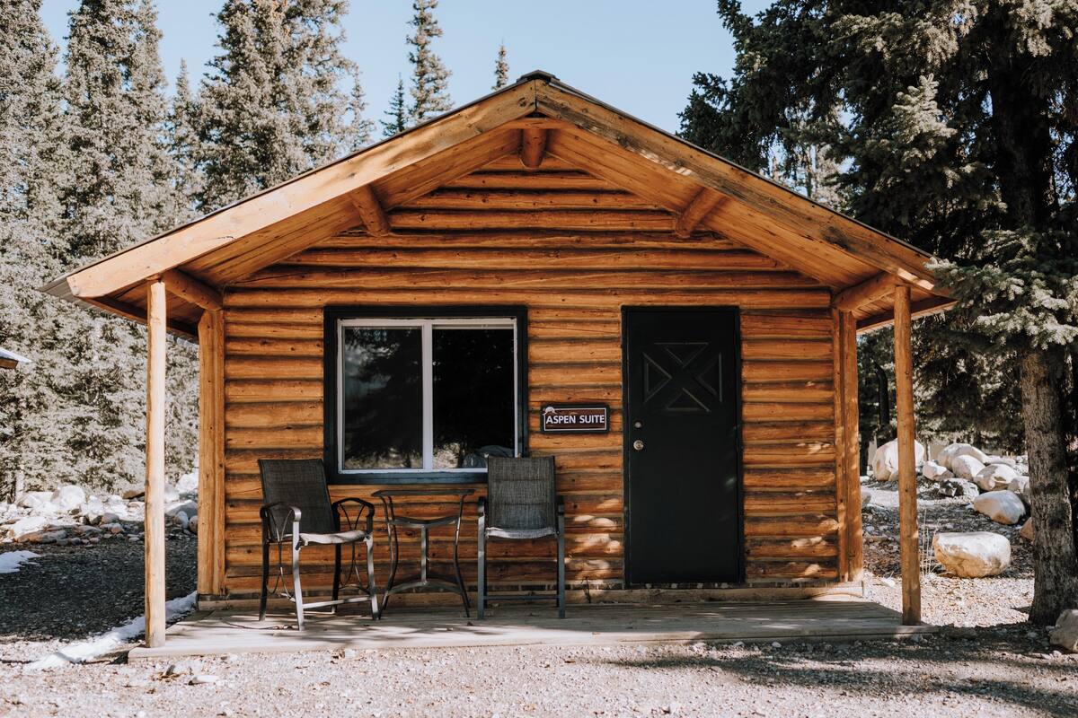 Eine Holzhütte mit einem Schild, das "Aspen Suite" zeigt, zwei Stühlen vor der Tür.