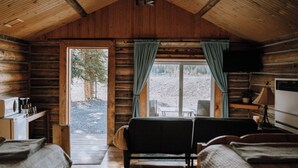 L’intérieur d’une cabane en rondins, avec un plafond en bois, un canapé, une table et un téléviseur.