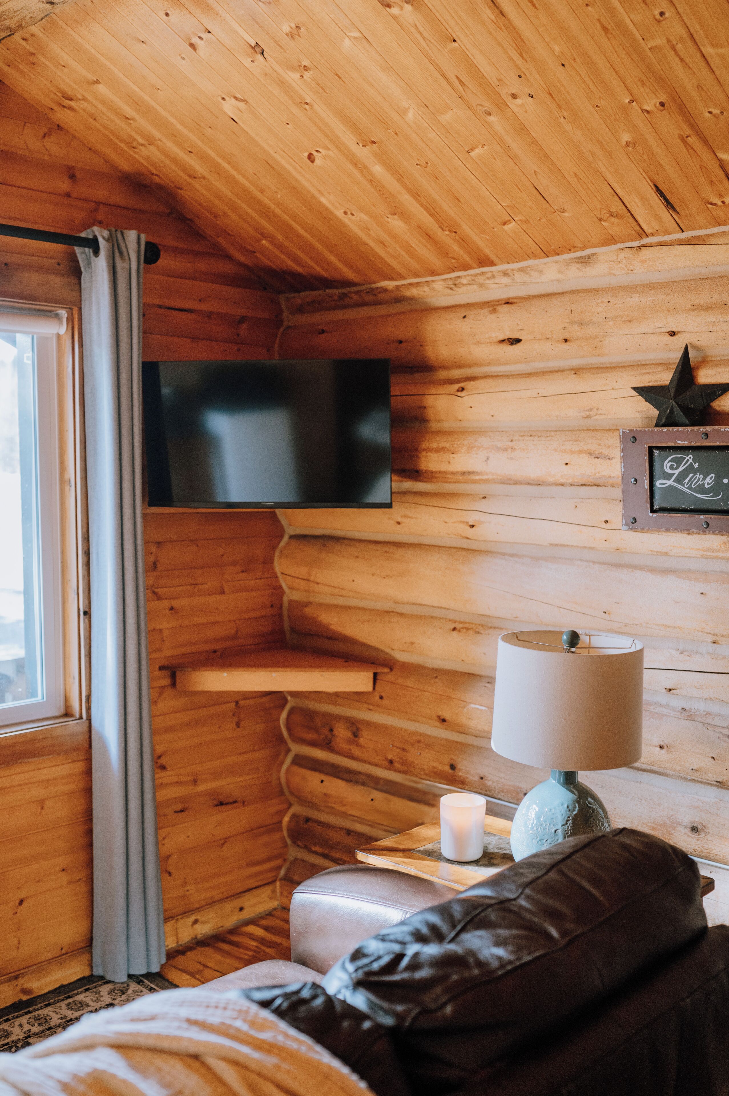 Ein Holzblockhaus-Innenraum mit an der Wand montiertem Fernseher, einer Lampe, einer Kerze und einer Lederbank.