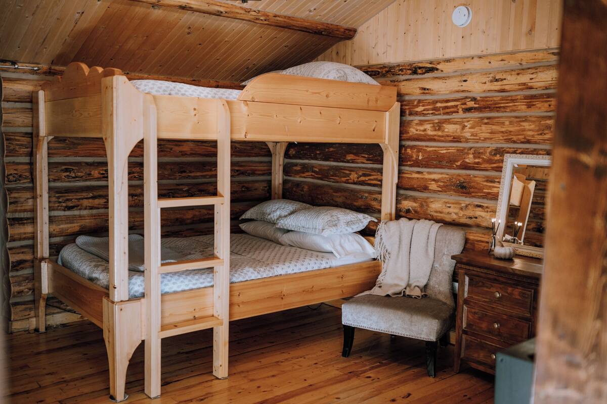 Ein Holzbett mit zwei Hängematten in einem Blockhausszimmer mit Stuhl und Kommode.