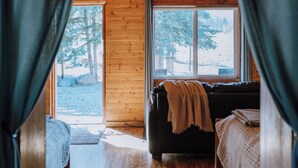 L’intérieur d’un chalet accueillant, avec un plancher en bois, un canapé recouvert d’une couverture et une fenêtre donnant sur le paysage extérieur.