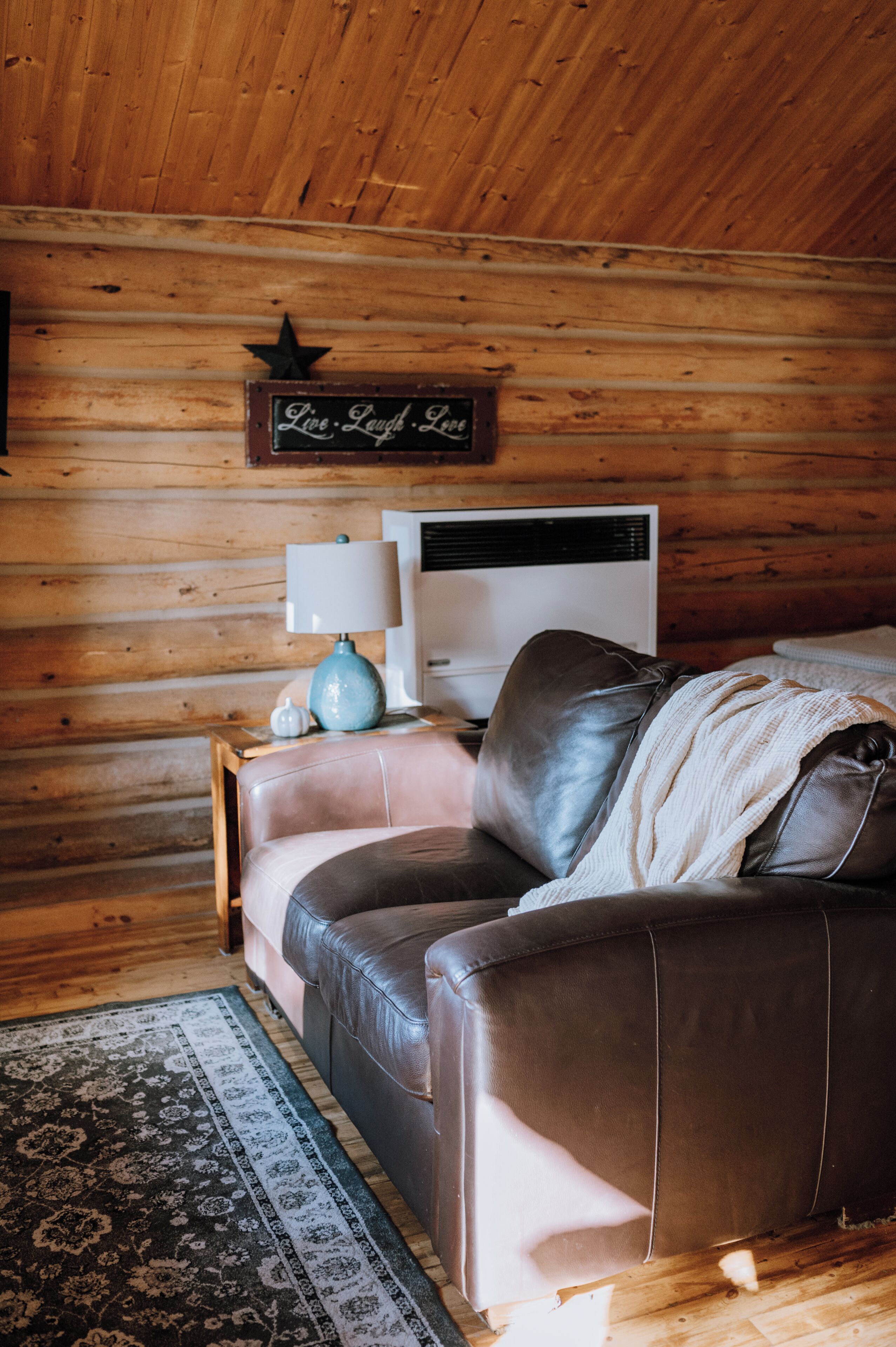 L’intérieur chaleureux d’un chalet avec un canapé en cuir, une lampe, une décoration en forme d’étoile et un panneau sur lequel on peut lire : « Vivez, riez, aimez ».