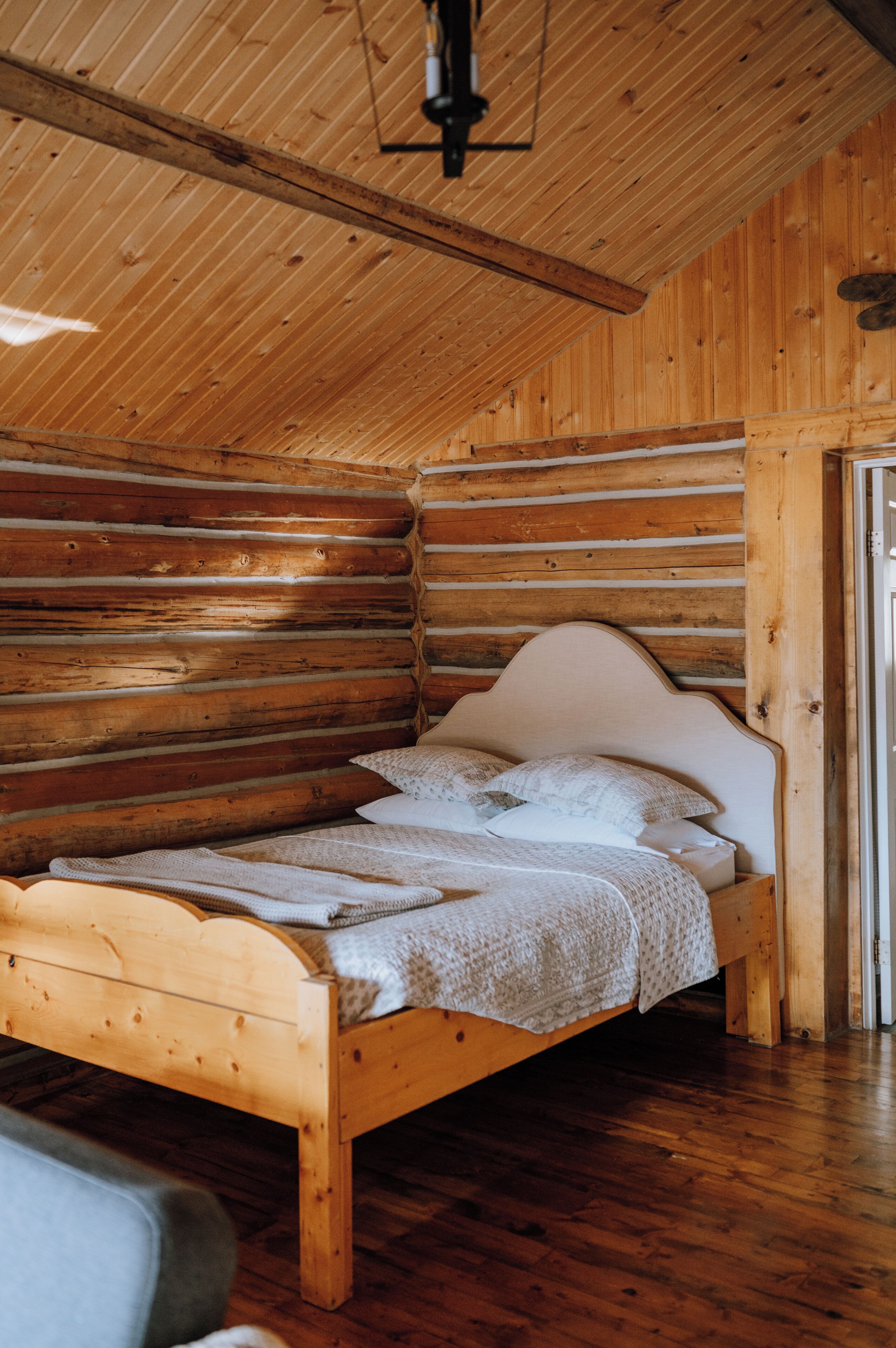 A wooden log cabin interior with a bed, wooden walls, and a sloped ceiling.