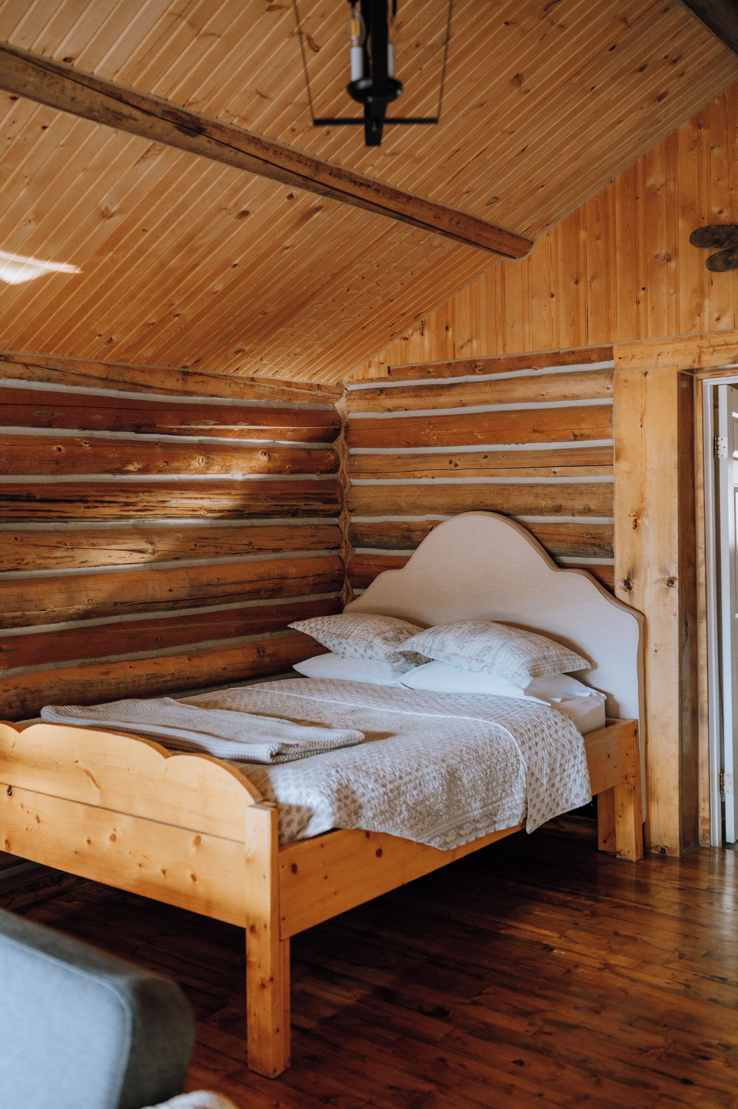 A wooden log cabin interior with a bed, wooden walls, and a sloped ceiling.