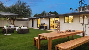 Un patio exterior moderno con mesa y bancos de madera, una parrilla y un césped bien cuidado.