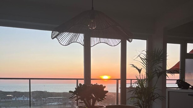 A dining area with a table and chairs, a potted plant, and a view of the sunset over the ocean.