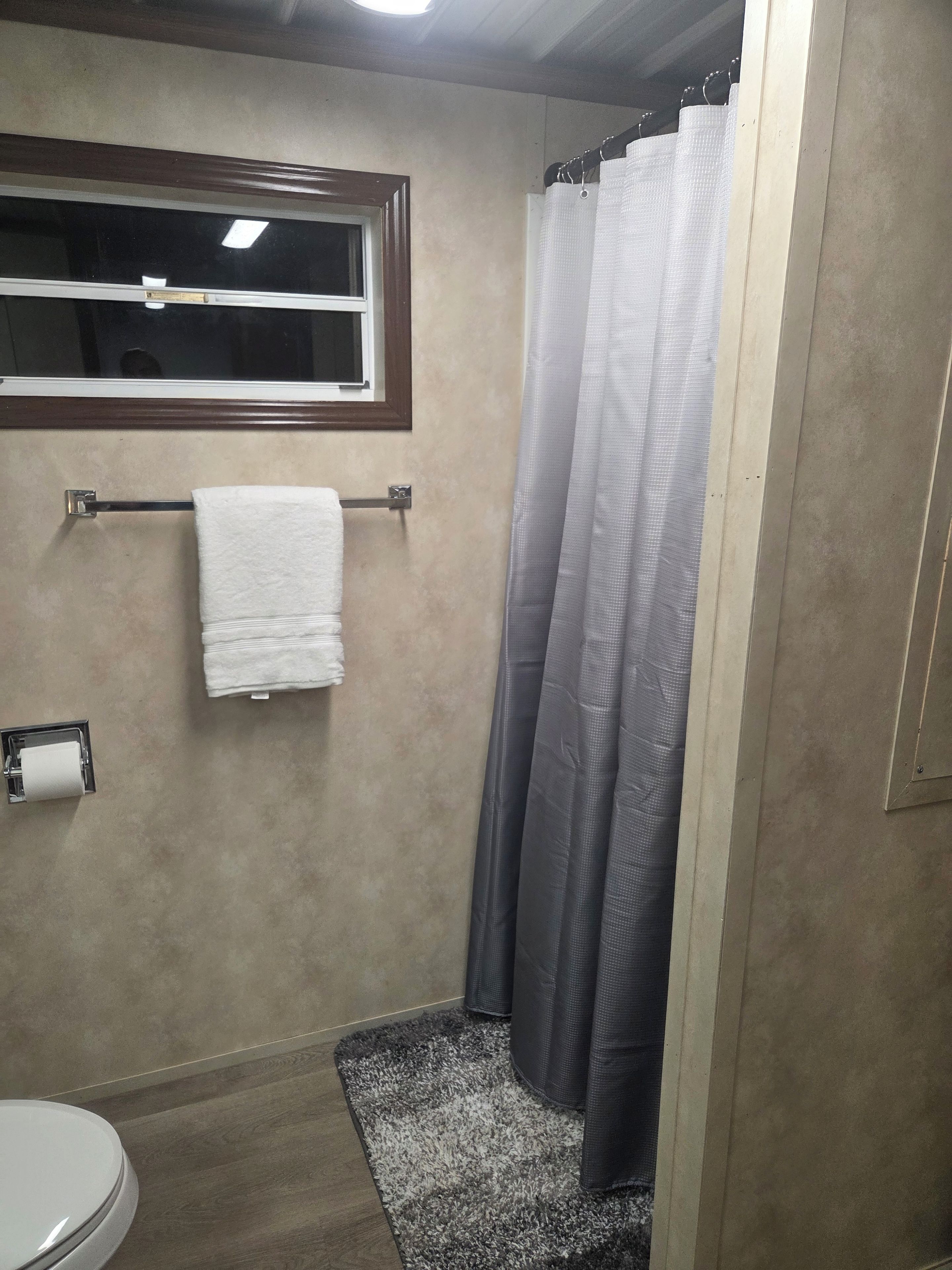 A bathroom with a toilet, a towel rack with a white towel, a shower curtain, and a small rug on the floor.