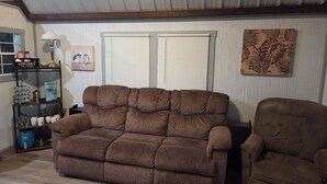 Ein Wohnzimmer mit einem braunen Sofa, einem braunen Sessel, einer Kaffeestation und einem Gemälde an der Wand.