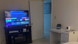 A bedroom with a bed, a TV on a stand, a desk, and a door leading to another room. - Your Penn State Destination pt 3 (State College)