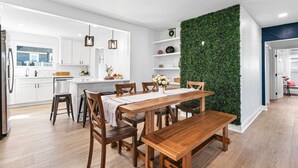 Une cuisine moderne avec des meubles blancs, une table à manger en bois et un mur végétal vertical vert.
