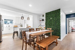 Una cocina moderna con armarios blancos, una mesa de comedor de madera y un jardín vertical verde.