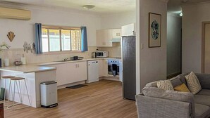 A modern kitchen with white cabinets, a microwave, and a refrigerator. There is a grey sofa with patterned cushions in the living area. - Your Pet Friendly Home Away From Home In Yeppoon | Sleeps 10 (Yeppoon)