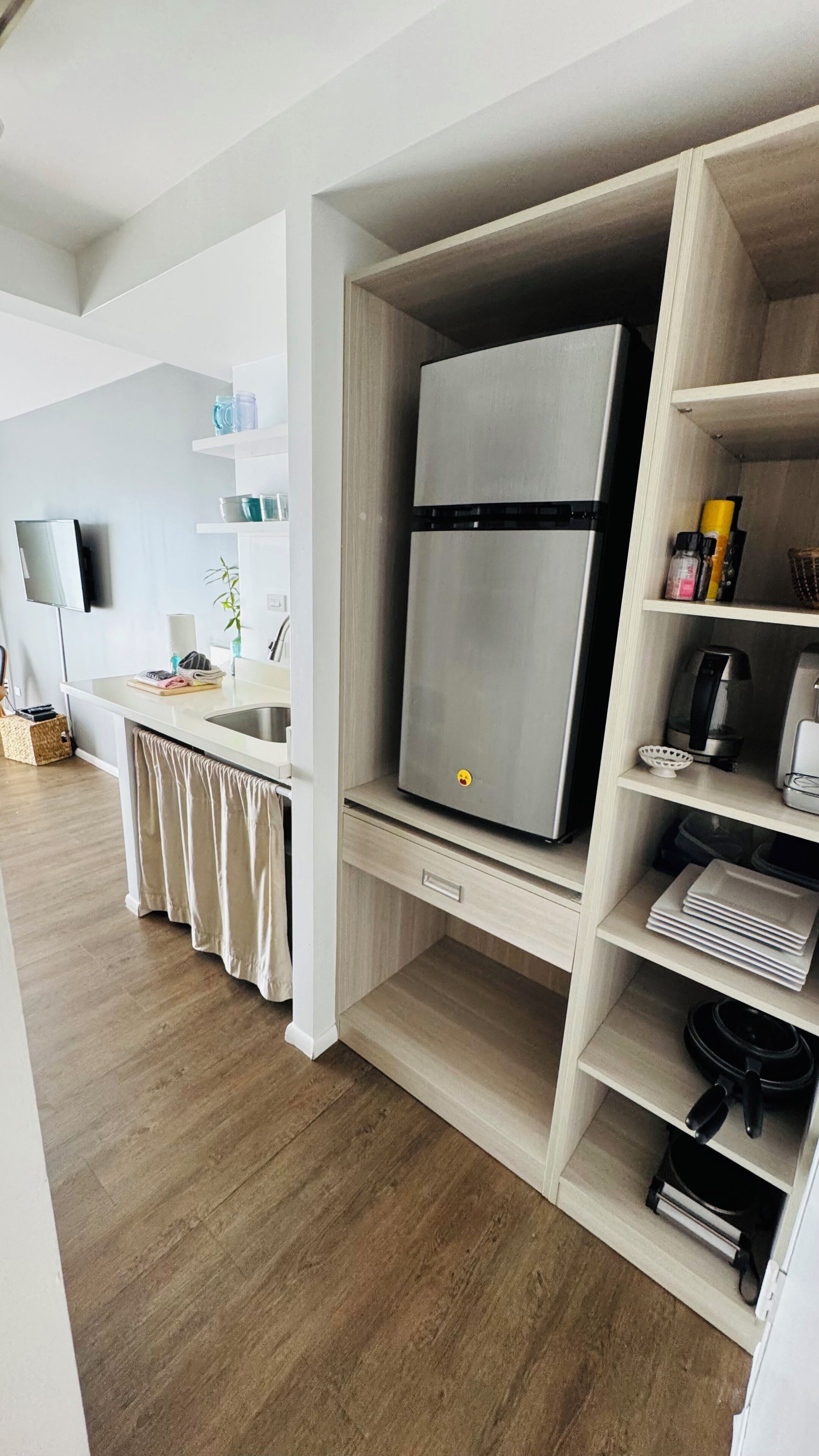 Eine moderne Küche mit einem eingebauten, Edelstahl-Kühlschrank, Holzschränken und einem flachbildfernseher an der Wand.