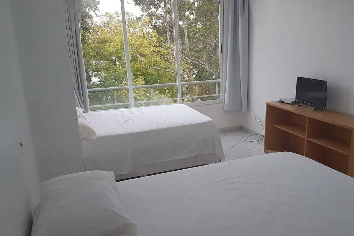 Une chambre avec deux lits, une fenêtre avec des rideaux et un téléviseur posé sur une étagère en bois.