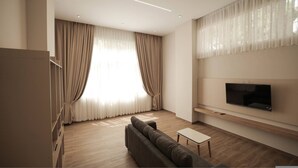 A modern living room with a large flat-screen TV mounted on the wall, a dark-colored sofa, a small white table, and a wooden floor. - Duplex City 08 in Durr s (Durrës)