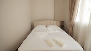 A neatly made bed with white linens and towels, a headboard, and a window with curtains. - Duplex City 05 in Durr s (Durrës)