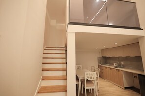 Una cucina moderna con mobili in legno, un'area pranzo con sedie bianche e una scala che conduce a un piano superiore.