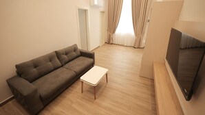 A living room with a sofa, a small table, a flat-screen TV, and a door. - Duplex City 05 in Durr s (Durrës)
