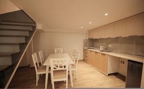 Una cucina moderna con mobili in legno, un lavello in acciaio inossidabile e una zona pranzo con tavolo e sedie bianche.