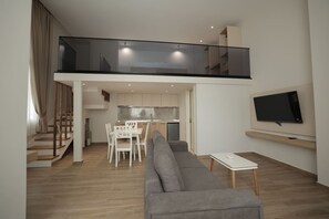 Ein zeitgemäßer Wohnbereich mit grauem Sofa, einem Esstisch, einer Küchenzeile und einem an der Wand montierten Fernseher.