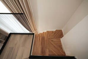 Eine Holztreppe mit modernem Design, die zu einem Raum mit weißen Wänden und einem Fenster mit beigen Vorhängen führt.
