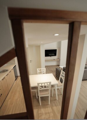 Eine moderne Küche mit Holzschränken, einem weißen Esstisch und Stühlen. Über der Sitzecke ist ein Fernseher an der Wand befestigt.
