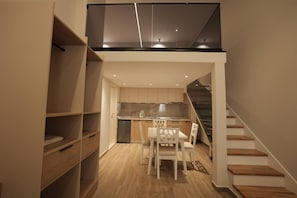 A modern kitchen with wooden cabinets, a dining area with white chairs, and a staircase leading to an upper level. - Duplex City 02 in Durr s (Durrës)