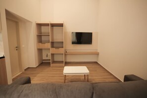 Ein kompakter Wohnbereich mit flachbildfernseher an der Wand, einem kleinen weißen Tisch und einem grauen Sofa.