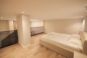 Une chambre moderne avec un grand lit, une balustrade en verre et un escalier menant à une autre pièce.