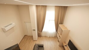 A modern living room with a sofa, a flat-screen TV, a wooden floor, and a window with curtains. - Duplex City 03 in Durr s (Durrës)