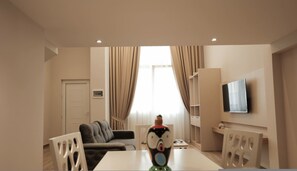 A modern living room with a sofa, a dining table, and a TV mounted on the wall. - Duplex City 03 in Durr s (Durrës)