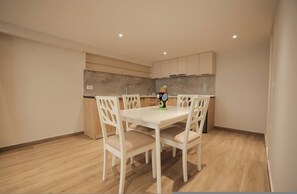 A modern kitchen with white cabinets, a white dining table with chairs, and a small island with a sink. - Duplex City 03 in Durr s (Durrës)
