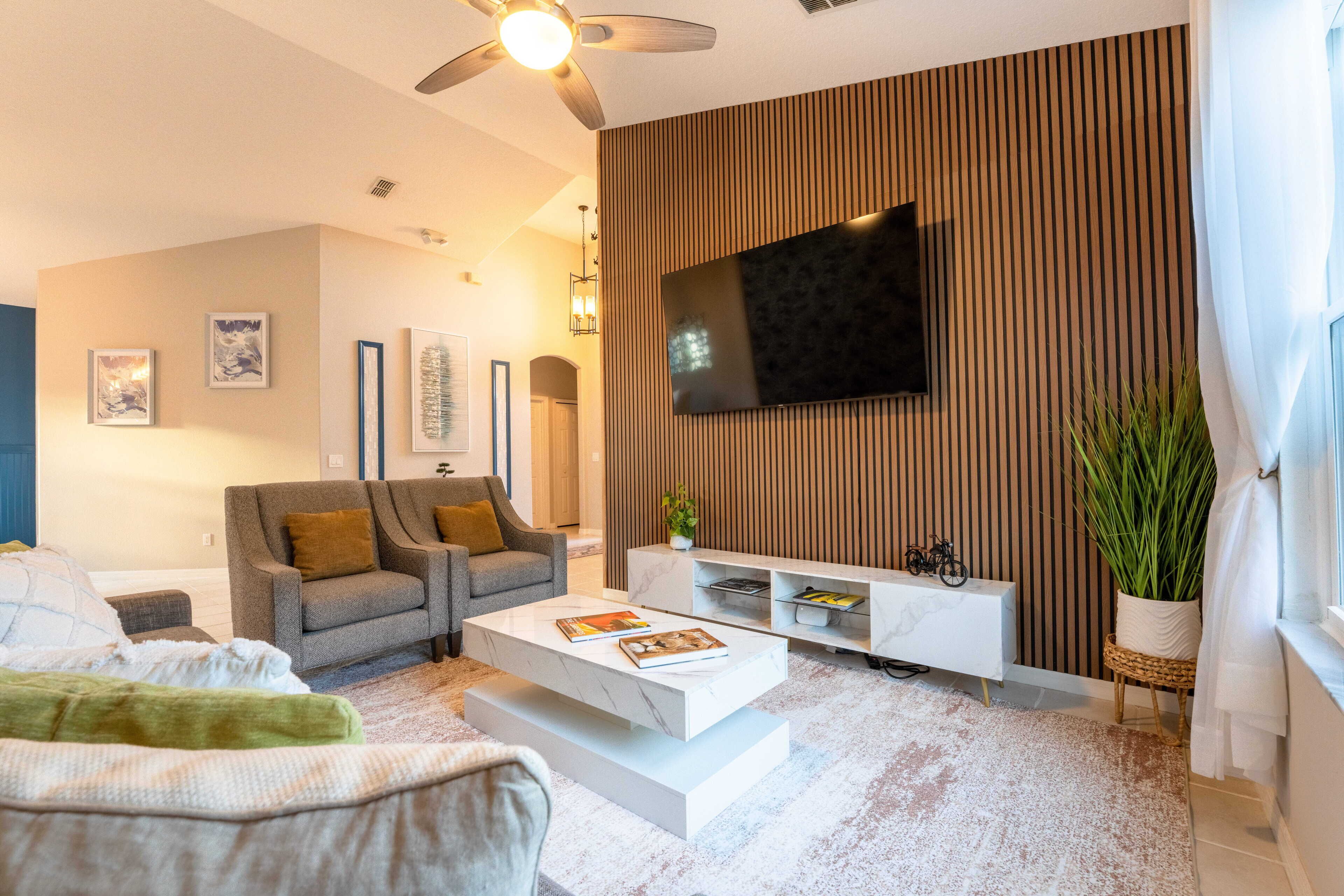 A modern living room with a flat-screen TV mounted on a wooden wall, a sofa, a coffee table, and a white console unit.
