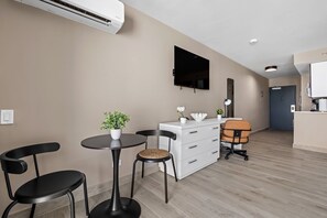 Ein modernes Hotelzimmer mit Flachbildfernseher, einem weißen Schminktisch, einem runden Esstisch mit zwei Stühlen und einer kleinen Topfpflanze.
