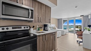 Une cuisine moderne équipée d’un four à micro-ondes, d’une cuisinière et d’une machine à café. Un balcon offre une vue sur la mer.