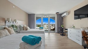 Une chambre d’hôtel avec deux lits, un bureau, une chaise, une télévision et un balcon avec vue.