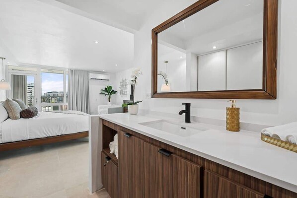 Ein modernes Schlafzimmer mit einem großen Bett, einer weißen Schminkkommode mit Spiegel und Blick auf die Stadt durch große Fenster.