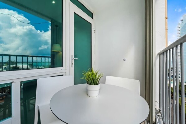 A balcony with a white table and chairs, a potted plant, and a view of the cityscape. - Isla Verde Beachfront Luxury Retreat (Carolina)