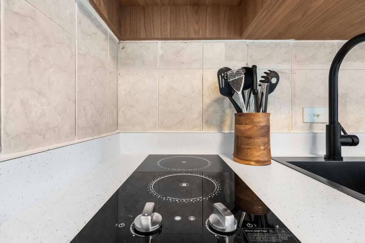 Una cocina con tope de inducción negro, un portalapices de madera y un grifo negro.