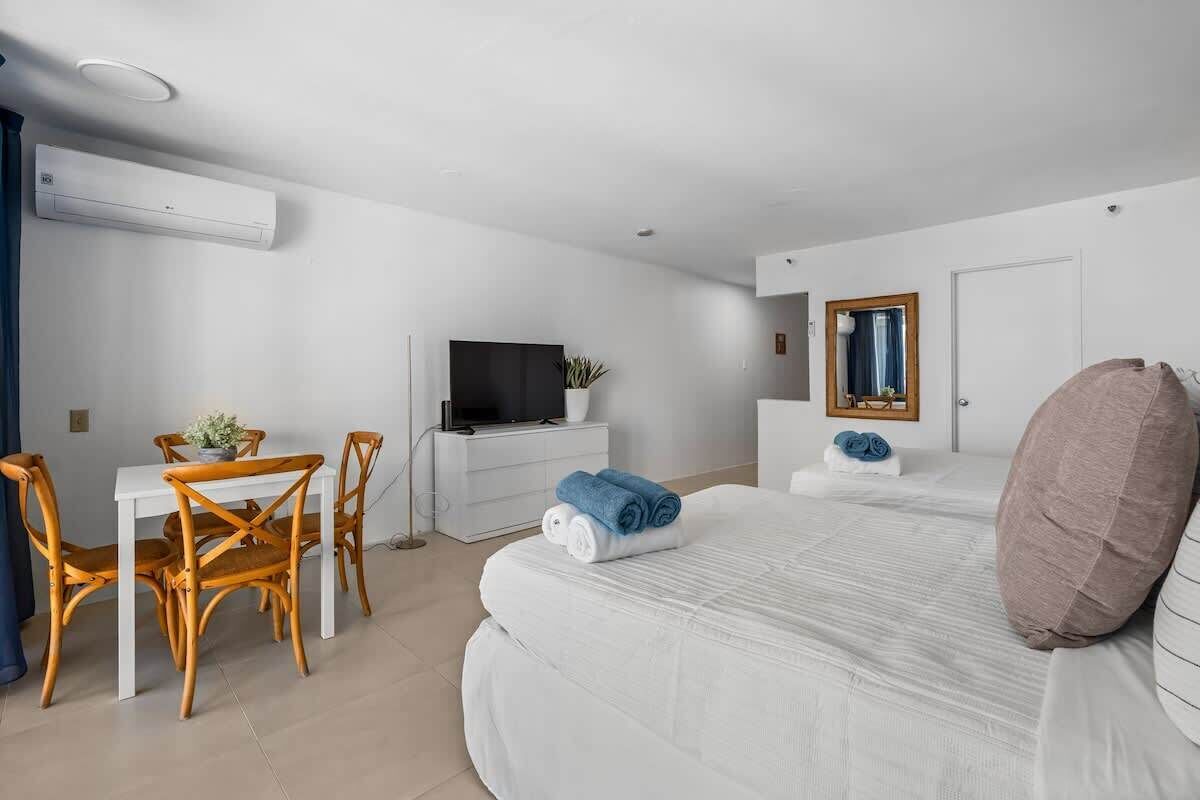 Ein Hotelzimmer mit einem Bett, einem Fernseher, einem Schreibtisch mit Stühlen und einem kleinen Tisch mit einer Pflanze.