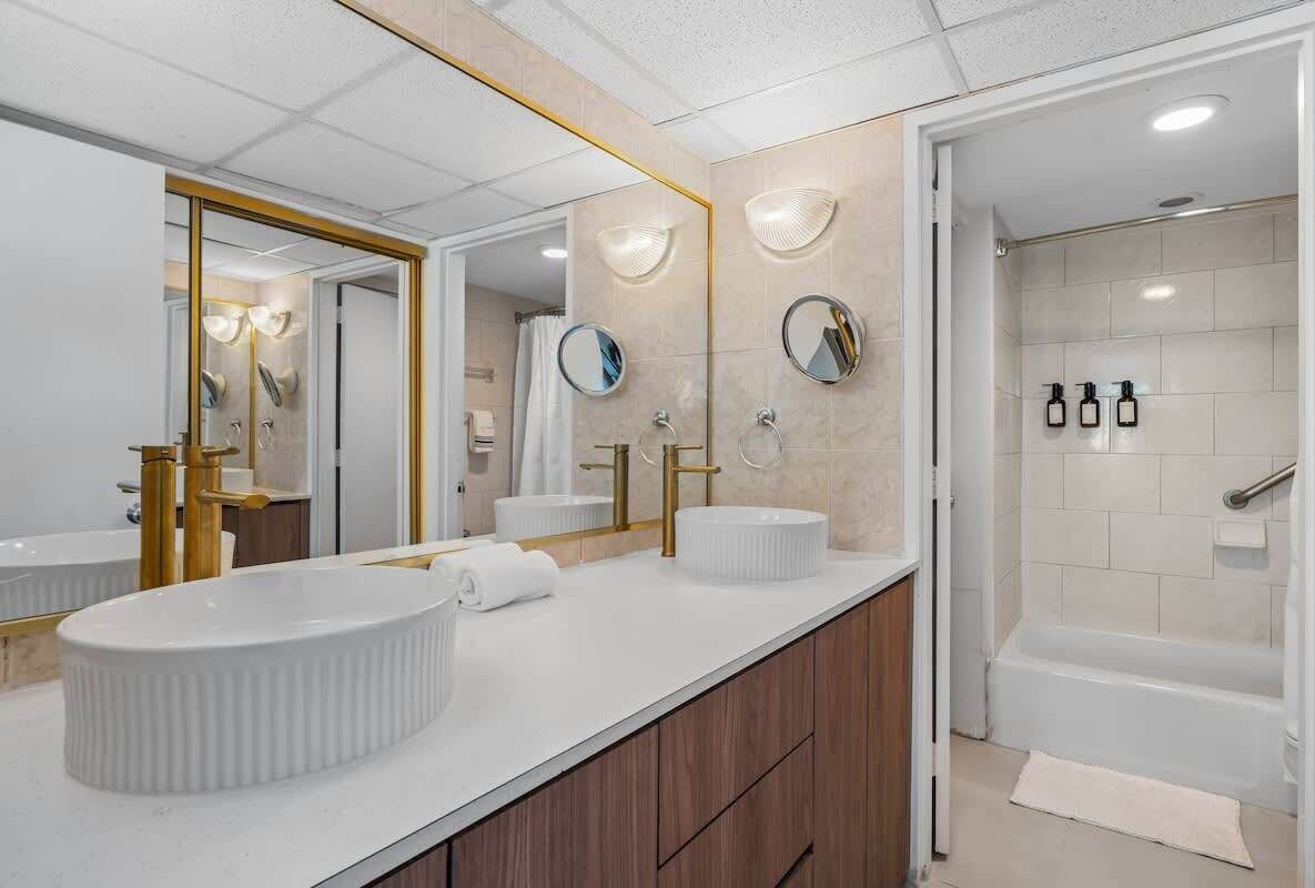 A modern bathroom with two sinks, a large mirror, and a shower area.