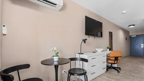 Een moderne kamer met een flatscreen televisie, een bureau met stoel, een klein tafeltje met een plant in pot en een witte dressoir.