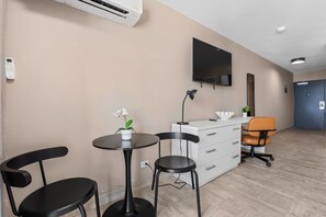 Ein modernes Zimmer mit Flachbildfernseher, Schreibtisch mit Stuhl, kleinem Tisch mit Blumentopf und weißem Schminktisch.