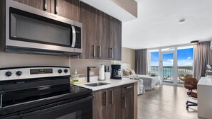 Een moderne keuken met een ingebouwde magnetron, kookplaat en gootsteen. Er is een klein eiland met een koffiezetapparaat en uitzicht op het balkon met een zwembad.