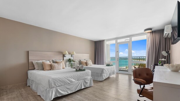 Een hotelkamer met twee bedden, een bureau en een stoel. Er is een groot raam met uitzicht op zee.