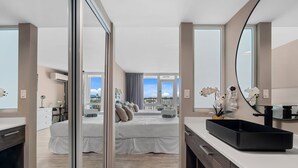 Een moderne hotelkamer met een groot bed, een badkamer met een zwarte wastafel en uitzicht op de stad.